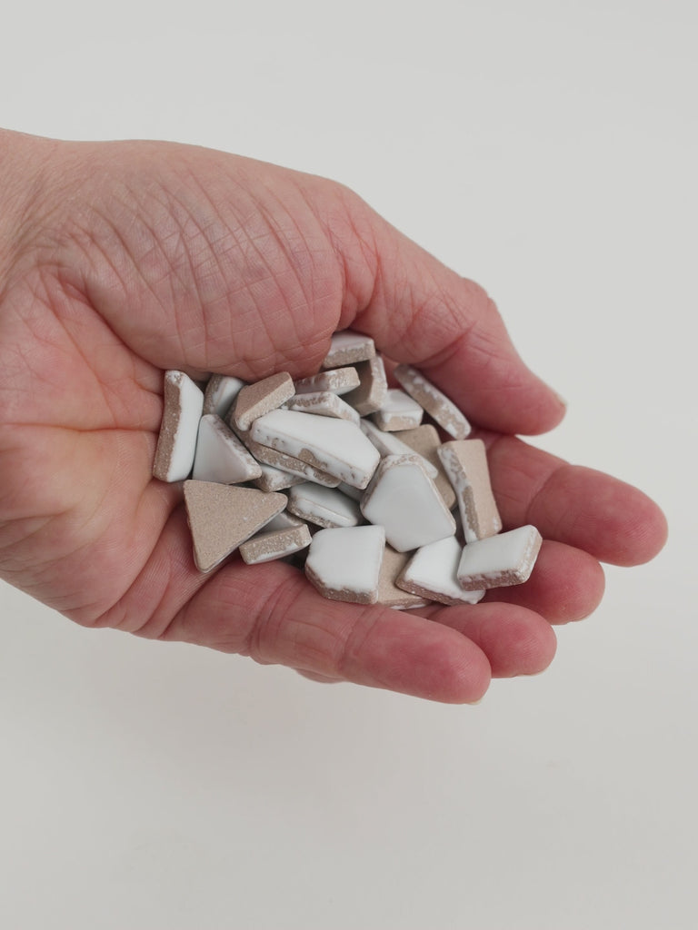 Video of Flip ceramic puzzle pieces in white, opaque glazed porcelain, 4–20 mm, held in a hand and poured out to show their shapes and finish